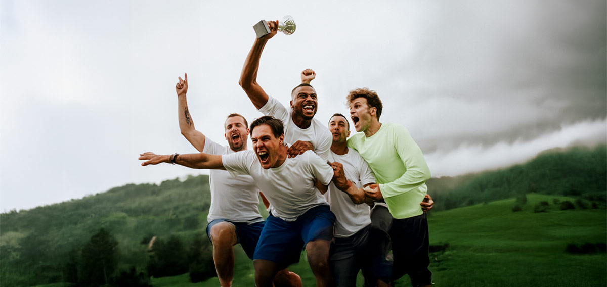 male teammates celebrating outside, holding trophy