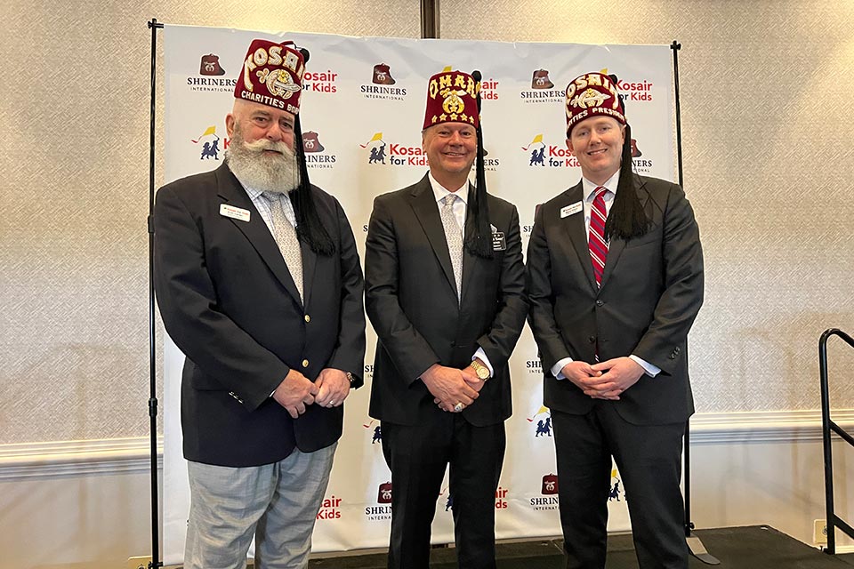 three Shriners stand in front of Kosair for Kids/Shriners International step and repeat